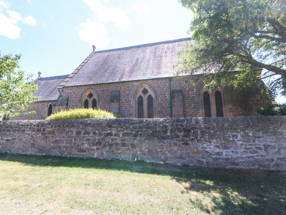 An old stone building with arched windows behind a stone wall and trees at Dale Cottage in Ingleton County Durham