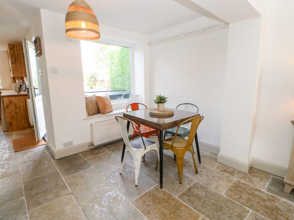 A dining area with a square table and four multicolored chairs near a window with cushions at Dale Cottage in Ingleton County Durham