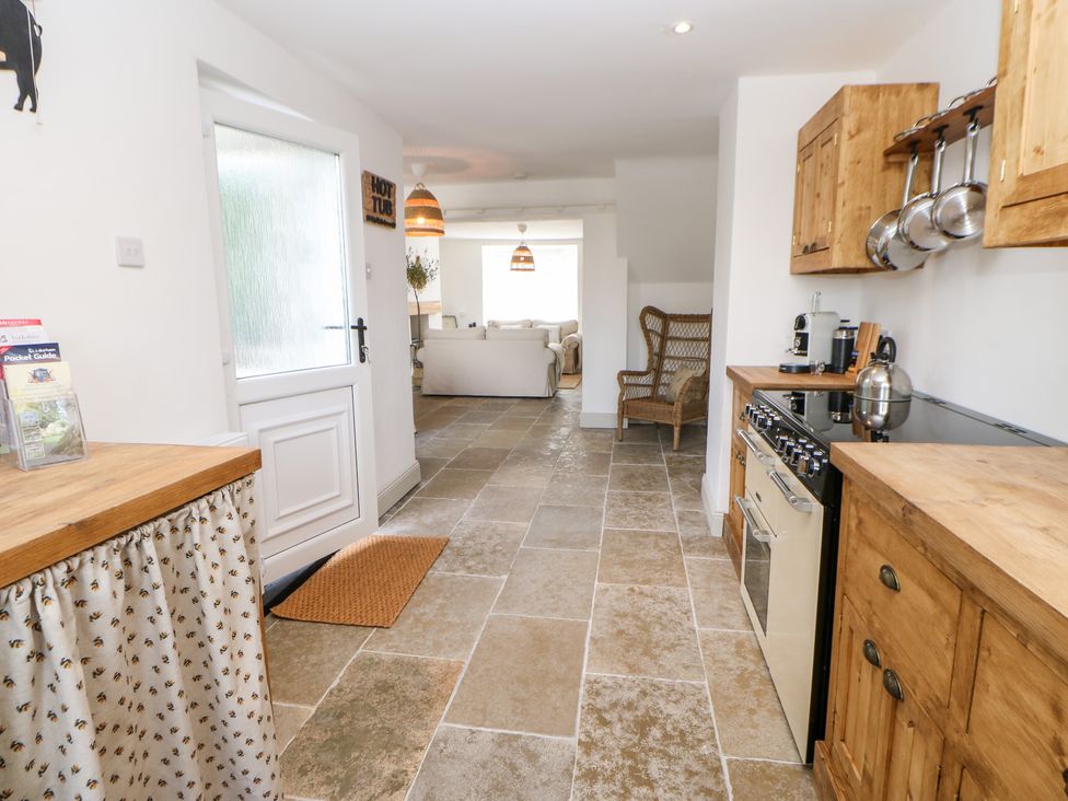 A kitchen with wooden cabinets stove and a wicker chair leading to a living room with sofas at Dale Cottage in Ingleton County Durham