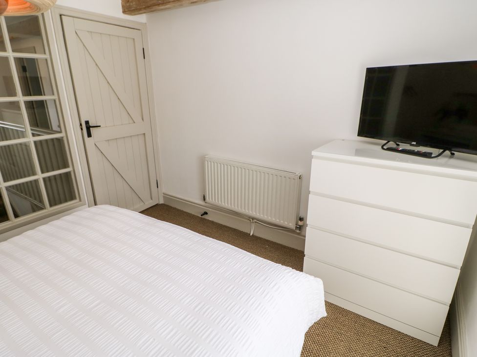 A bedroom with a white bedspread a white dresser with a television and a beige door at Dale Cottage in Ingleton County Durham
