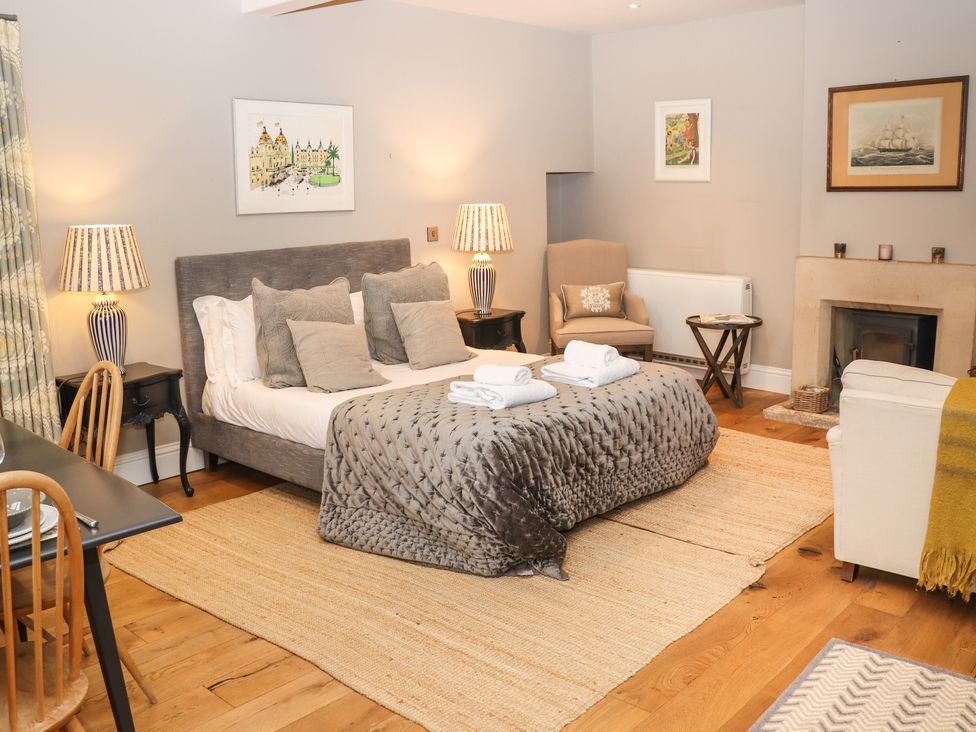 A bedroom with a bed with pillows and blankets two lamps a chair a table a fireplace and wall art at The Hermitage in Poulton