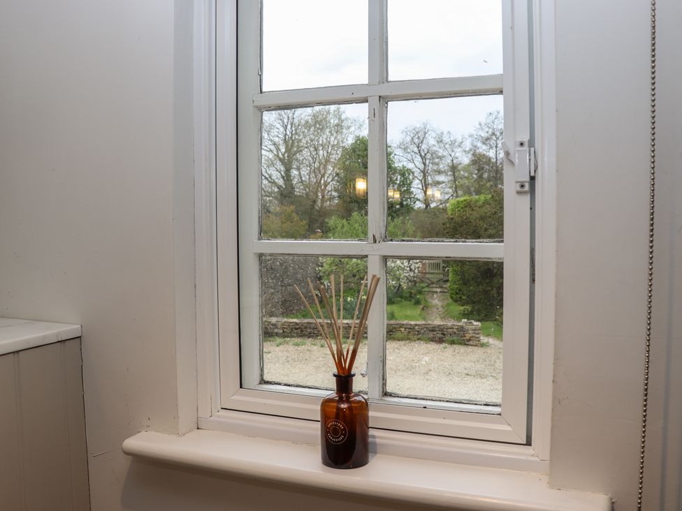 A window with white frame and a small brown bottle with reed diffuser sticks on the sill overlooking a garden with trees and a stone wall at The Hermitage in Poulton