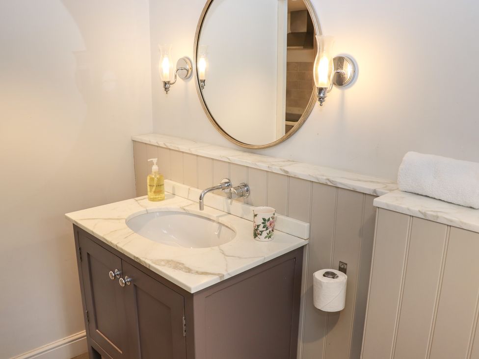 A bathroom sink with soap dispenser a floral cup and wall lights at The Hermitage in Poulton