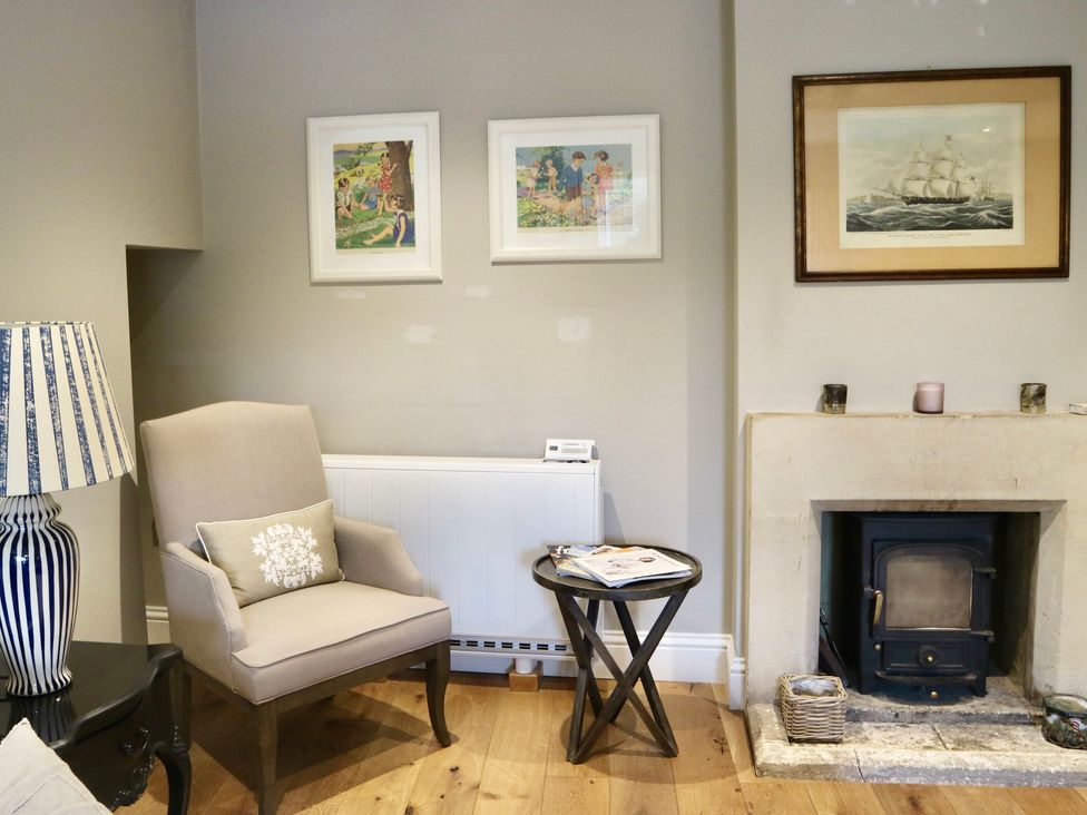 A room with an armchair beside a side table and a fireplace with framed pictures above at The Hermitage in Poulton