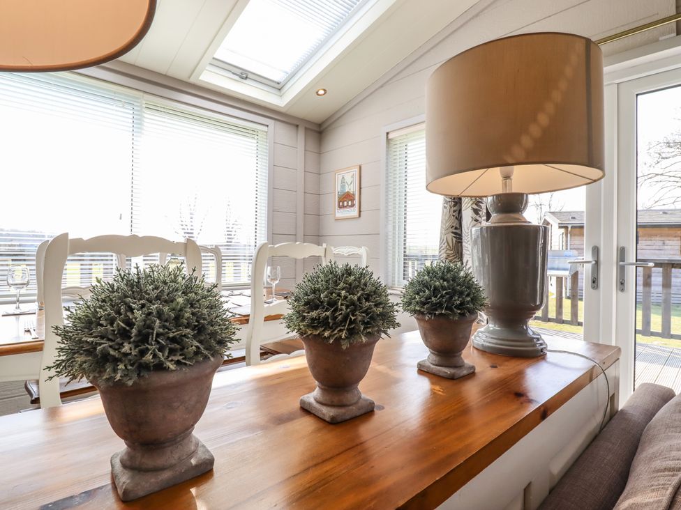 A wooden table with three potted plants and a lamp in a dining room with white chairs and windows at Skylarks in Fornham St Genevieve near Bury St Edmunds