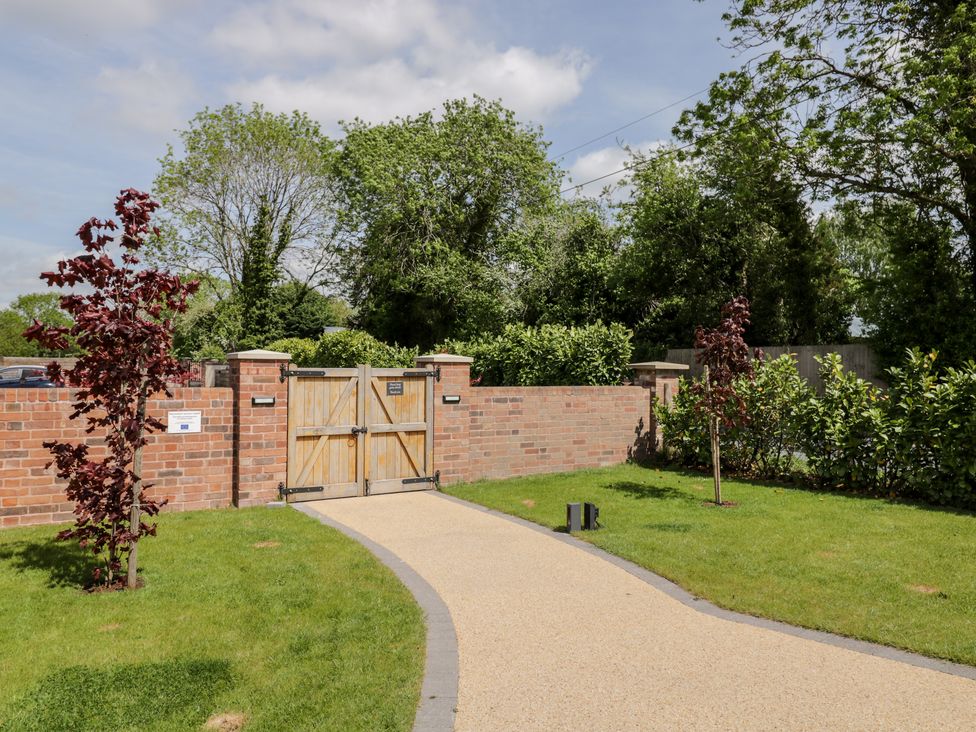 A driveway leading to wooden gates set in a brick wall with grass and small trees on both sides at Little Lugg in Cross Keys near Hereford