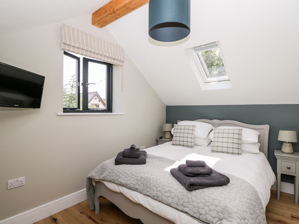 A bedroom with a double bed two bedside tables with lamps a window a skylight and a mounted TV at Little Lugg in Cross Keys near Hereford