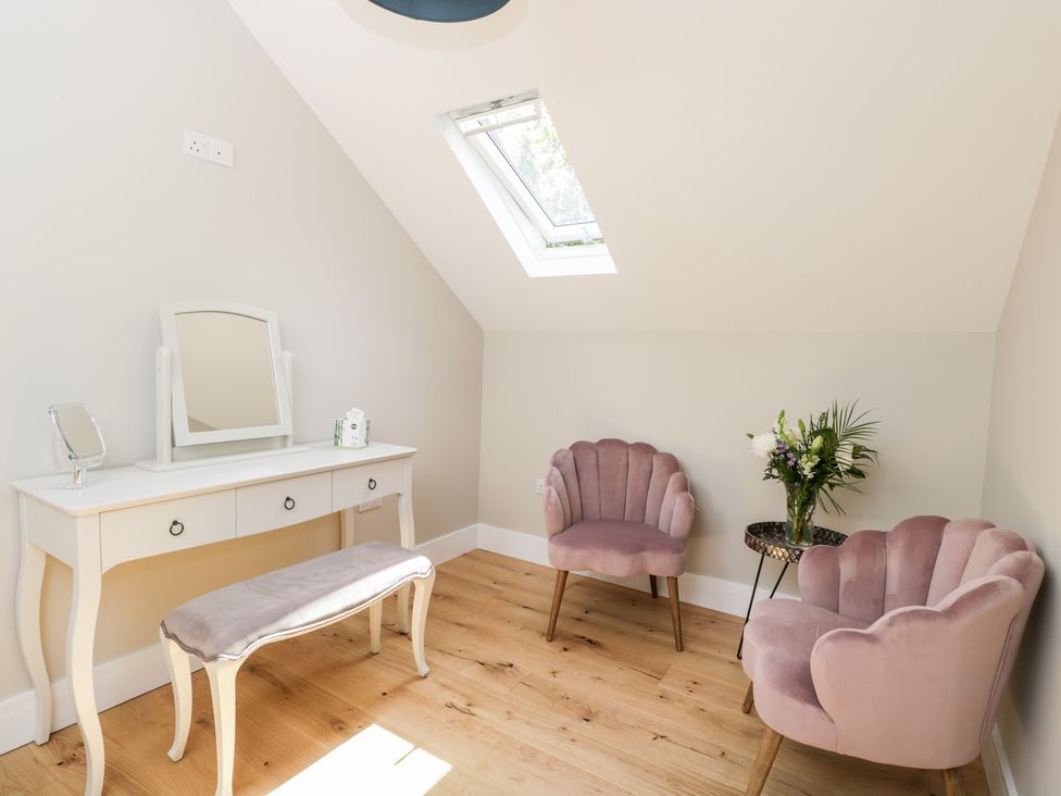 A room with a dressing table with mirror and bench and two pink upholstered chairs and a small round table with flowers at Little Lugg Cross Keys near Hereford