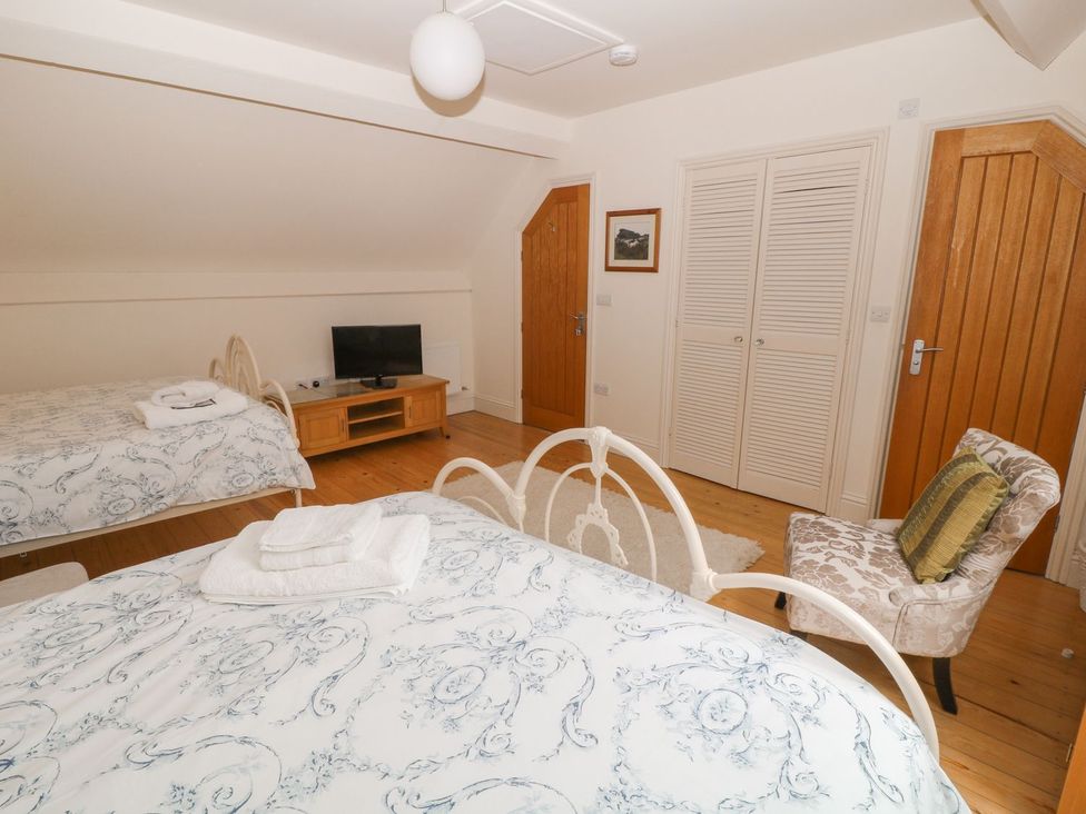 A bedroom with two beds a television on a wooden stand a chair and wooden doors at Higher Weddicott Barn in Chagford