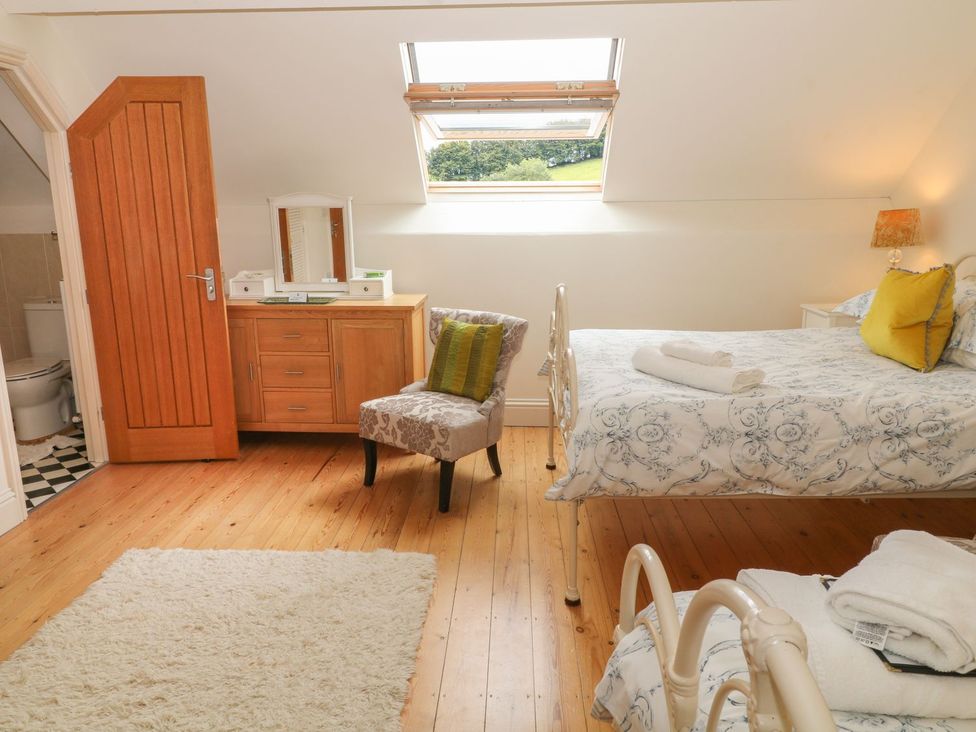 A bedroom with two beds a wooden dresser an upholstered chair a skylight window and an open door to a bathroom at Higher Weddicott Barn in Chagford