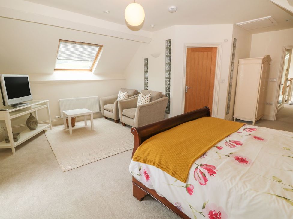 A bedroom with a bed a yellow throw and floral bedspread two armchairs a small table a television and a wardrobe at Higher Weddicott Barn in Chagford