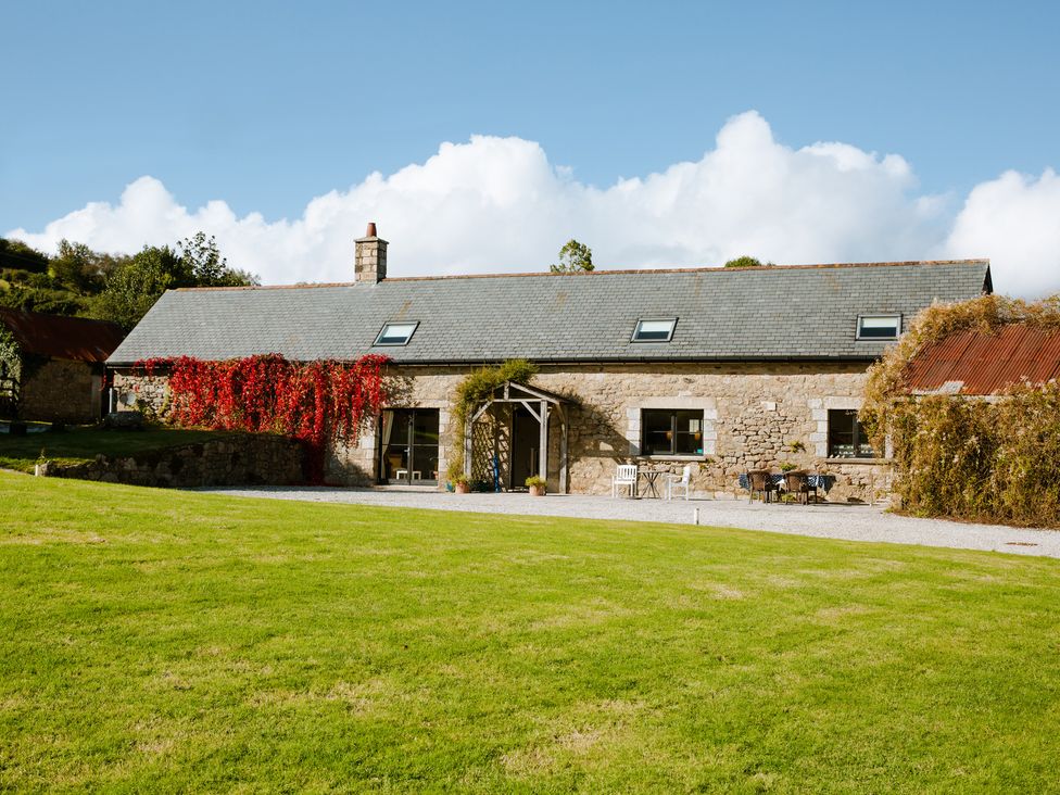 A stone barn with a slate roof surrounded by grass and climbing plants at Higher Weddicott Barn in Chagford