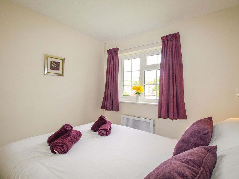 A bedroom with a bed with purple pillows and towels near a window with purple curtains and a vase with yellow flowers at West Lulworth Apartment in West Lulworth