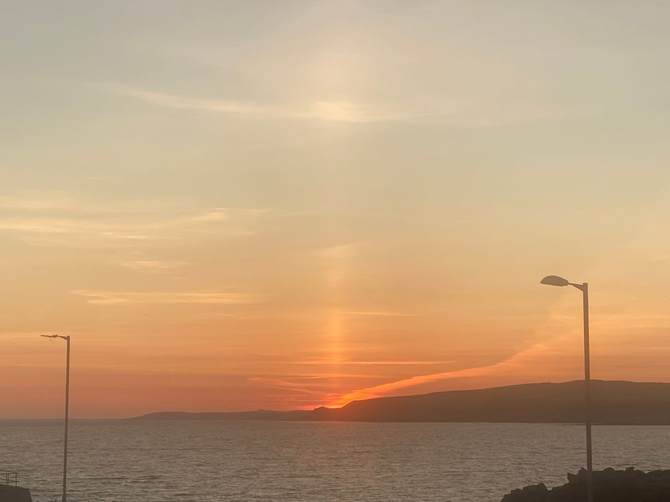 A sunset over the sea with hills in the distance and two street lamps at Westview in Whithorn