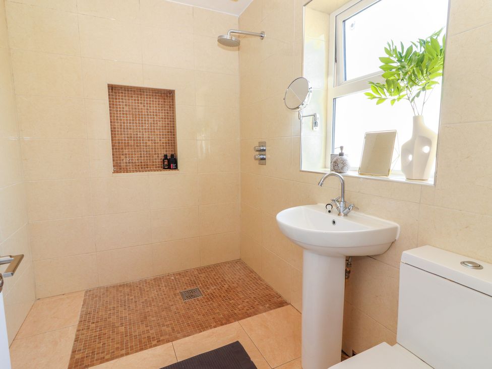 A bathroom with a walk-in shower, a pedestal sink, a toilet, and a window with decorative items on the sill at Cottage View in Moveen East near Kilkee County Clare