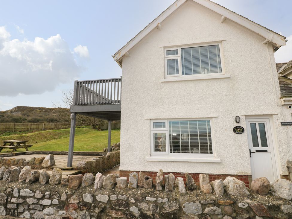 The exterior of a white two-story house with a stone wall and a picnic bench in a grassy yard at 2 Salt Cottage in Port Eynon