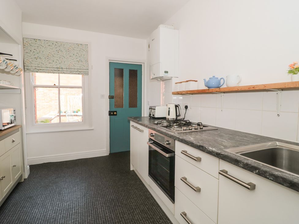 A kitchen with white cabinets a black countertop a gas stove an oven a sink and a blue door at Bluebell Apartment in Swanage