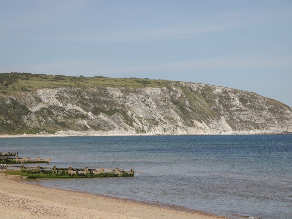 A beach with wooden groynes extending into the sea and cliffs covered with grass in the background at Bluebell Apartment in Swanage