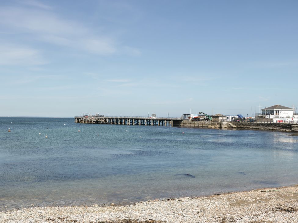 A pebble beach with a pier extending into the calm sea under a clear sky at Bluebell Apartment in Swanage