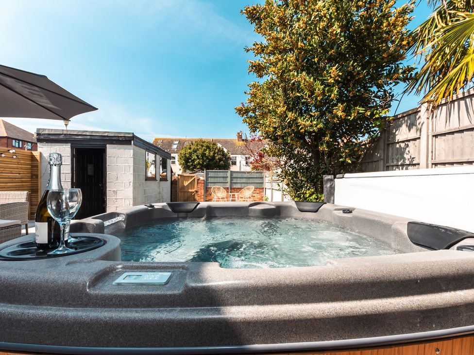 An outdoor patio with a hot tub a bottle of champagne and a glass two chairs under a tree at Anchor House in Weymouth