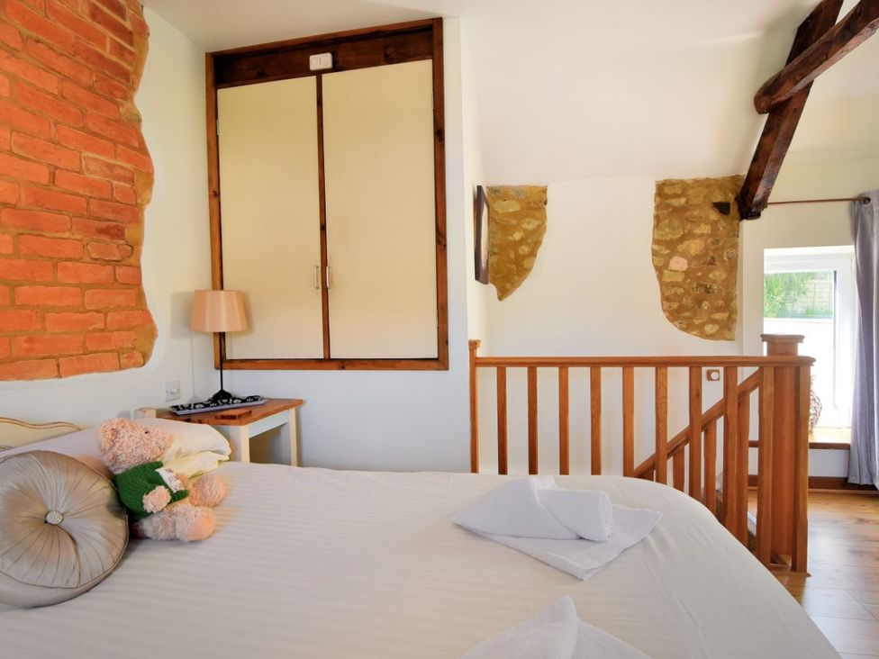 A bedroom with a bed with a teddy bear and pillows a wooden railing a small side table with a lamp and exposed brick and stone walls at The Flower Patch in Uplyme