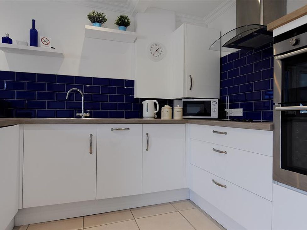 A kitchen with white cabinets blue tiled backsplash a microwave kettle and stovetop at 2 Mareeba Seaton