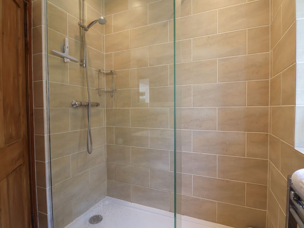 A tiled shower area with a glass partition a showerhead and a metal storage rack at 5 Belmont Terrace in Beer