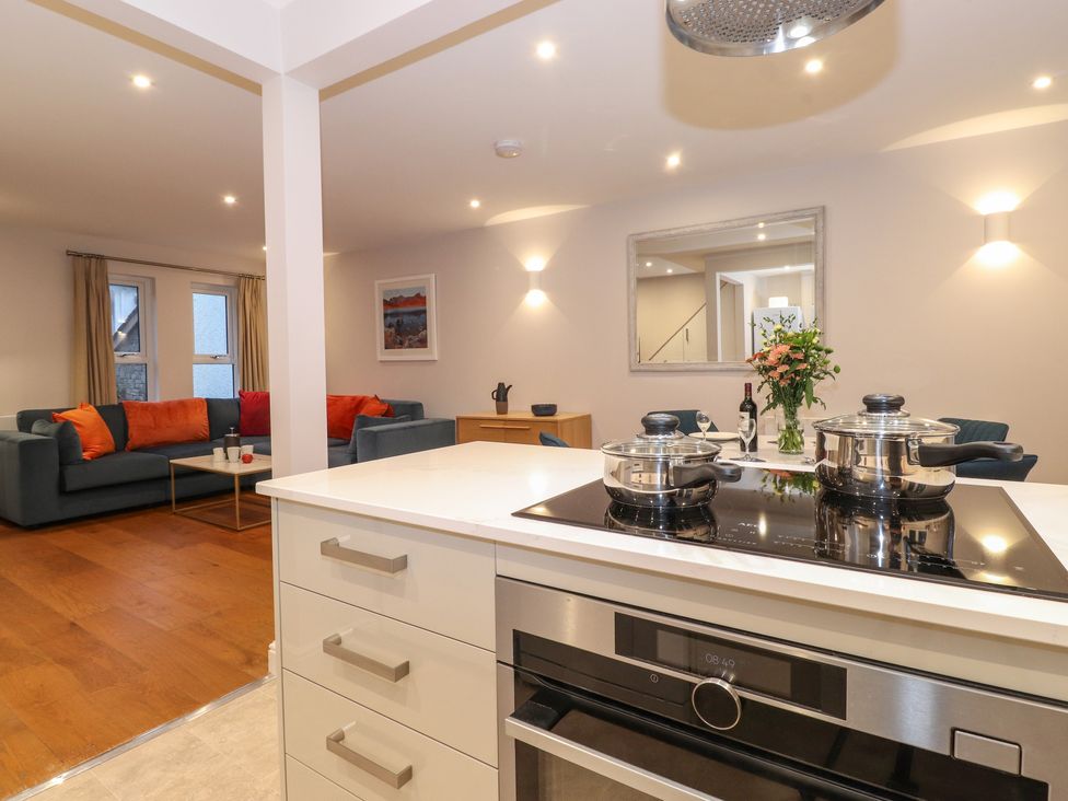 A kitchen with stove and pots overlooking a living room with blue sofas and orange cushions at Merry Bank in Ambleside