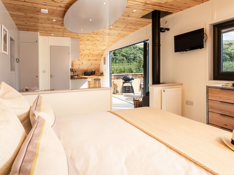 A bedroom with a bed and pillows facing a kitchen and an open door leading to an outdoor deck with a grill at Little Heaning in Cartmel