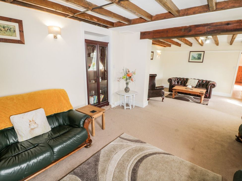 A living room with wooden beams on the ceiling two leather sofas a wooden coffee table a small wooden side table a cabinet with glass doors a round table with a vase of flowers and framed pictures on the walls at Woodlands Cottage in Snainton