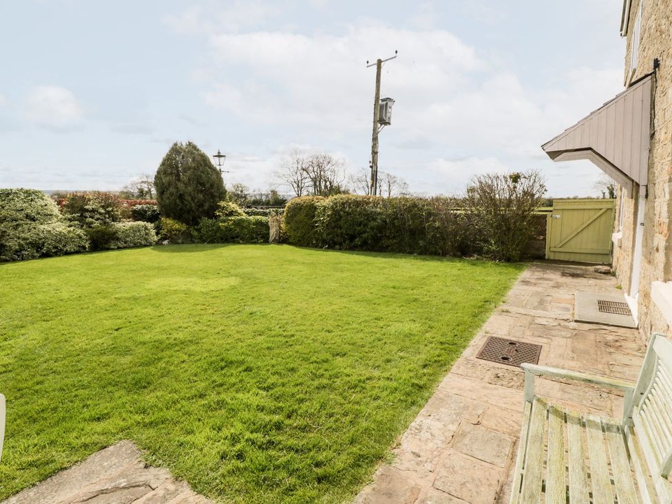 A fenced garden with grass and bushes next to a stone house at Woodlands Cottage in Snainton