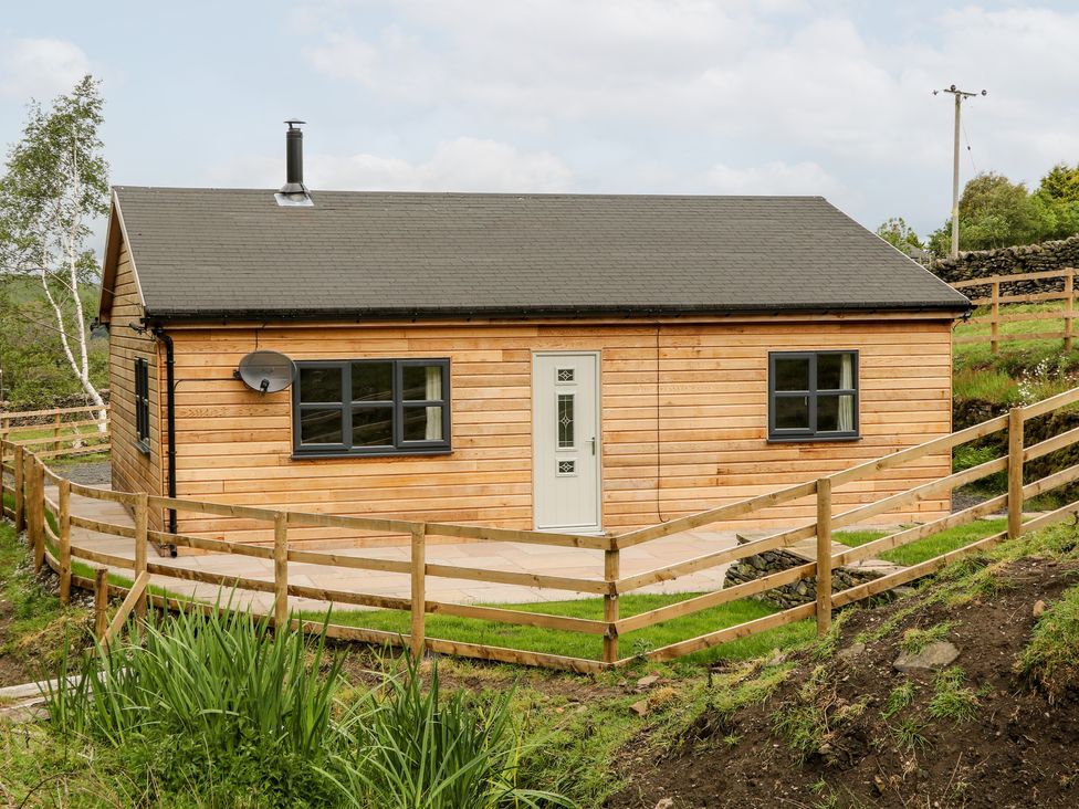 A wooden house with a fenced yard and a satellite dish at Brookside in Hayfield