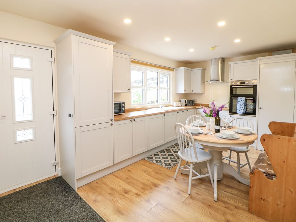 A kitchen with white cabinets a round dining table set with dishes and flowers at Brookside in Hayfield