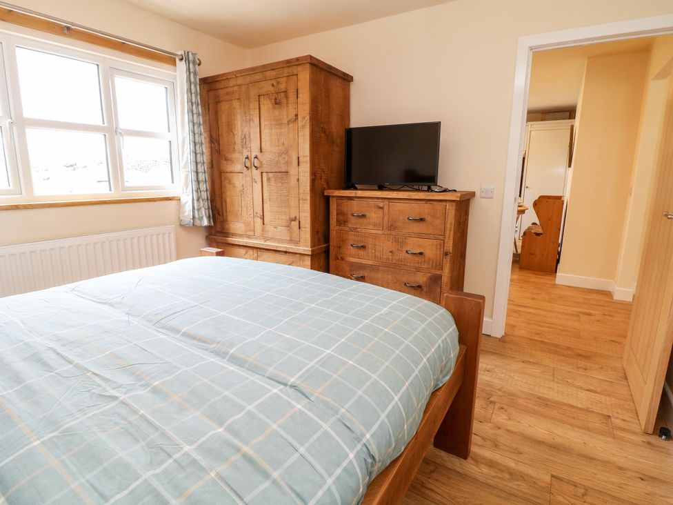 A bedroom with a wooden bed, a wooden wardrobe, a wooden chest of drawers with a television on top and a window with curtains at Brookside in Hayfield