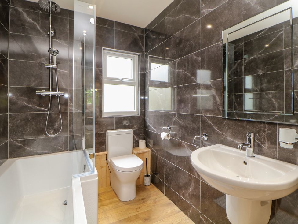 A bathroom with a bathtub shower combination a toilet a sink and a mirror at Brookside in Hayfield