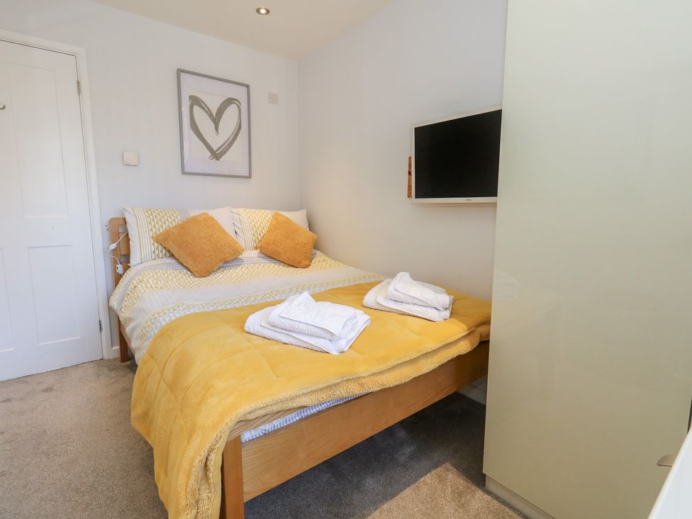 A bedroom with a double bed yellow pillows and blanket folded towels a wall mounted television and heart artwork at Swallow Lodge in Milford On Sea