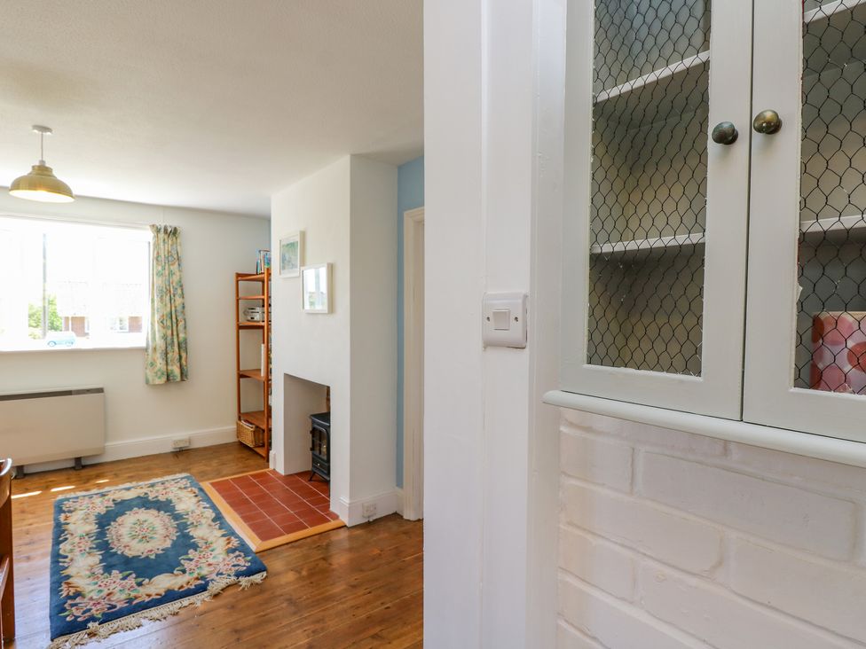 A living room with a rug a wood floor a fireplace and a window with floral curtains at Ladylands Cottage in Shorwell