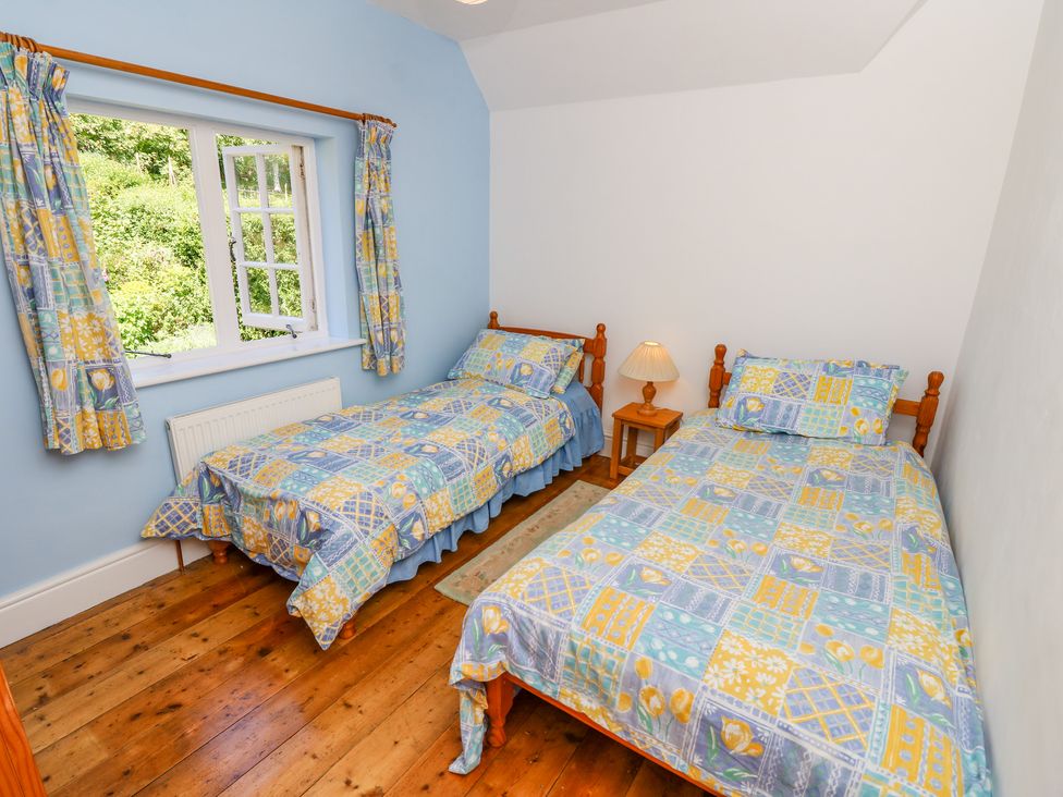 A bedroom with two single beds wooden floor a window with patterned curtains and a bedside table with a lamp at Ladylands Cottage in Shorwell