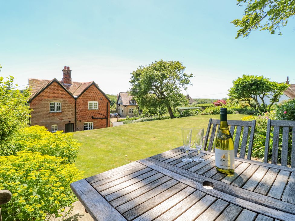 A garden with a wooden table and chairs a bottle of wine and two glasses near a brick house at Ladylands Cottage in Shorwell