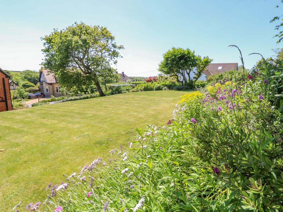 A garden with grass lawn flowers and trees with houses in the background at Ladylands Cottage in Shorwell