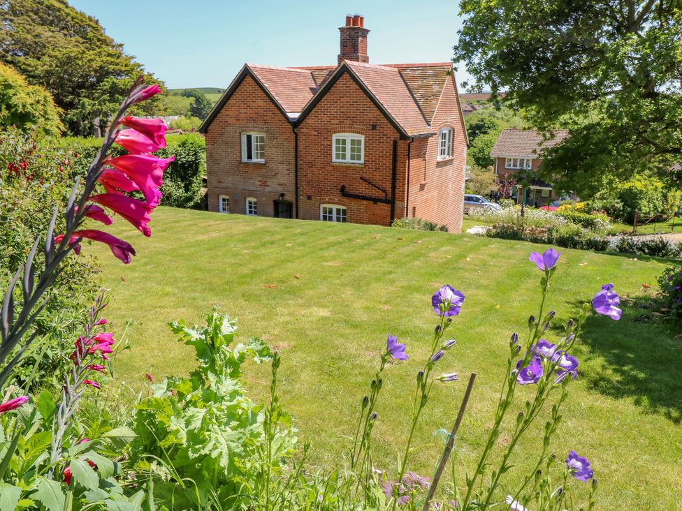 A brick house with a chimney surrounded by a lawn and flowers at Ladylands Cottage in Shorwell