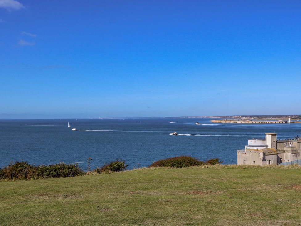 A grassy hill overlooking the sea with boats on the water and buildings along the shoreline at Ladylands Cottage in Shorwell