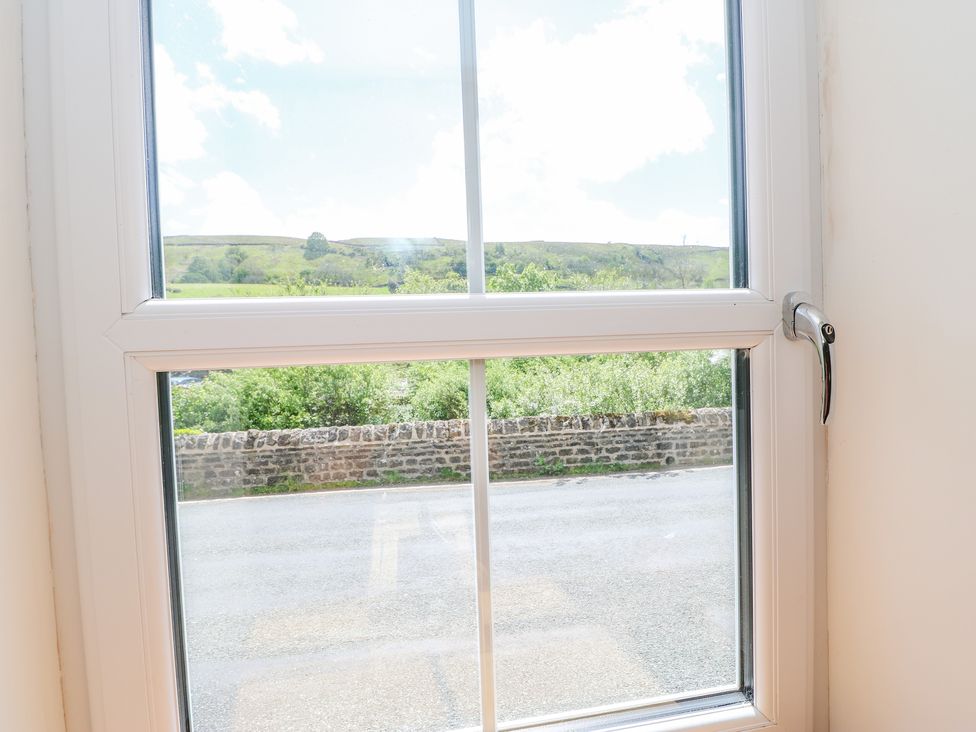 A window with a handle overlooking a stone wall a road and green hills at Wayside Farm in Muker