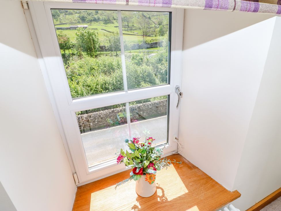 A window with a flower vase on the wooden sill overlooking a green landscape at Wayside Farm in Muker