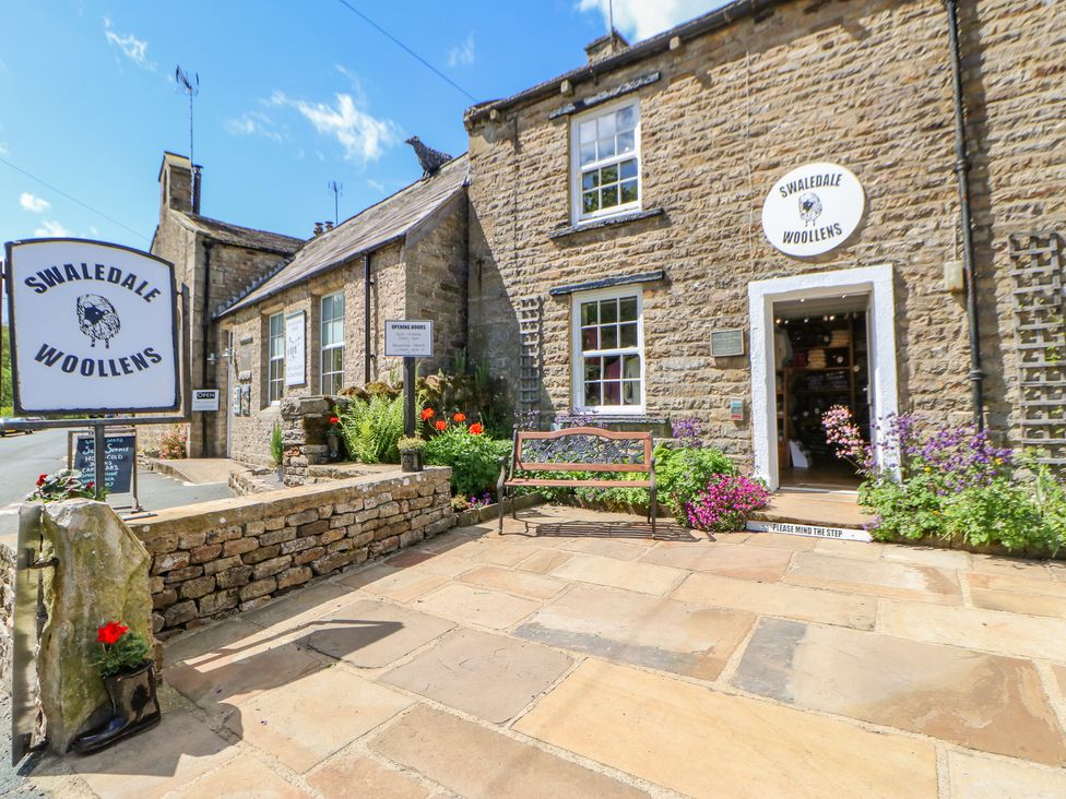 Stone building with flowers and a bench outside Swaledale Woollens in Muker