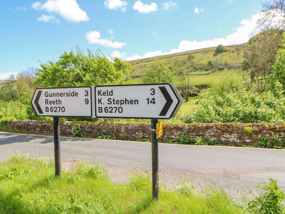 A road sign at a rural crossroads showing directions to Gunnerside Reeth Keld and K Stephen with green hills and stone wall in the background at Wayside Farm in Muker