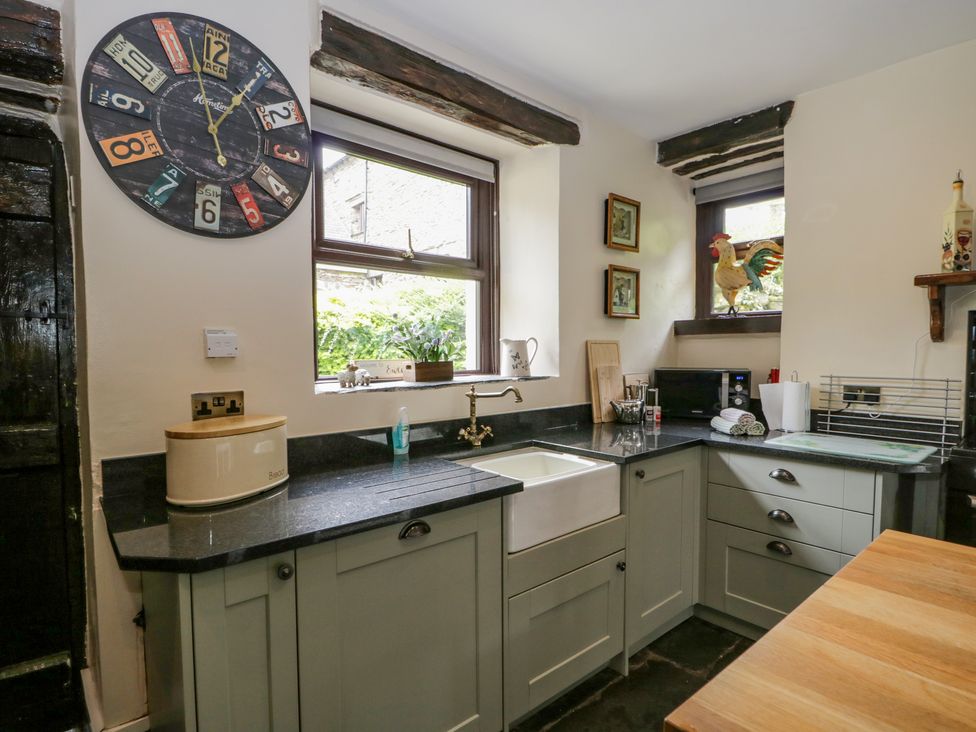 A kitchen corner with a black countertop a white sink and cabinets a colorful wall clock and two windows at Ewedale Farm Pennington near Ulverston