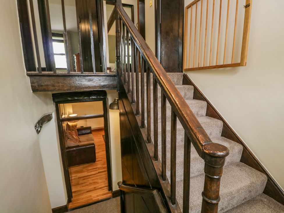 A staircase with dark wooden railing and carpet next to a doorway leading to a living room with a sofa and lamp at Ewedale Farm Pennington near Ulverston