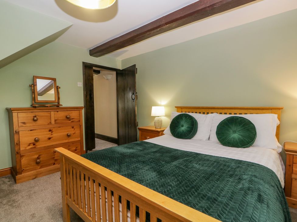 A bedroom with a wooden bed with green pillows and throw a wooden chest of drawers and bedside tables with lamps at Ewedale Farm Pennington near Ulverston