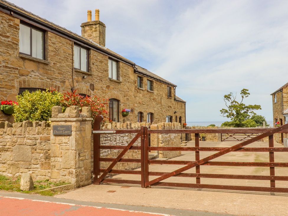 A stone building with windows and a chimney behind a wooden gate and stone wall at The Cottage @ Picton near Gwespyr